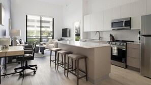 A modern kitchen with a central island, bar stools, a dining area with a table and chairs, and a view of the outdoors through large windows. - Landing | Modern 3BD, Gym, Yoga Studio (North Miami)