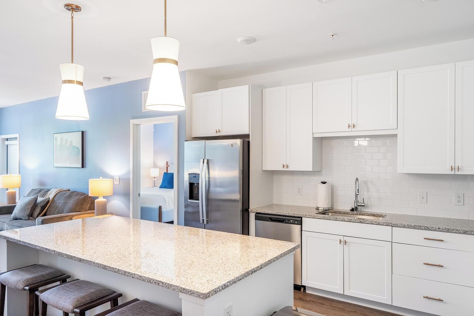 A modern kitchen with white cabinets, granite countertops, stainless steel appliances, and pendant lighting.