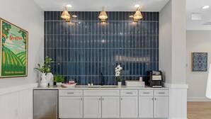 Cozinha moderna com armários brancos, painel de parede escuro e luminárias pendentes.
