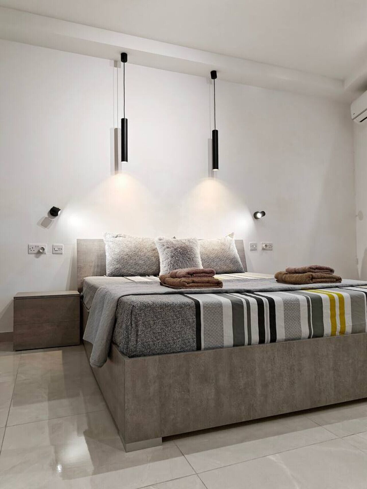 Une chambre moderne avec un grand lit, deux lampes suspendues et une table de chevet.