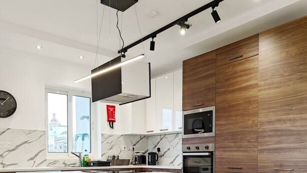 A modern kitchen with a marble island, wooden cabinets, and a built-in oven. - Valley view 1  2 bedroom aparment (Luqa)