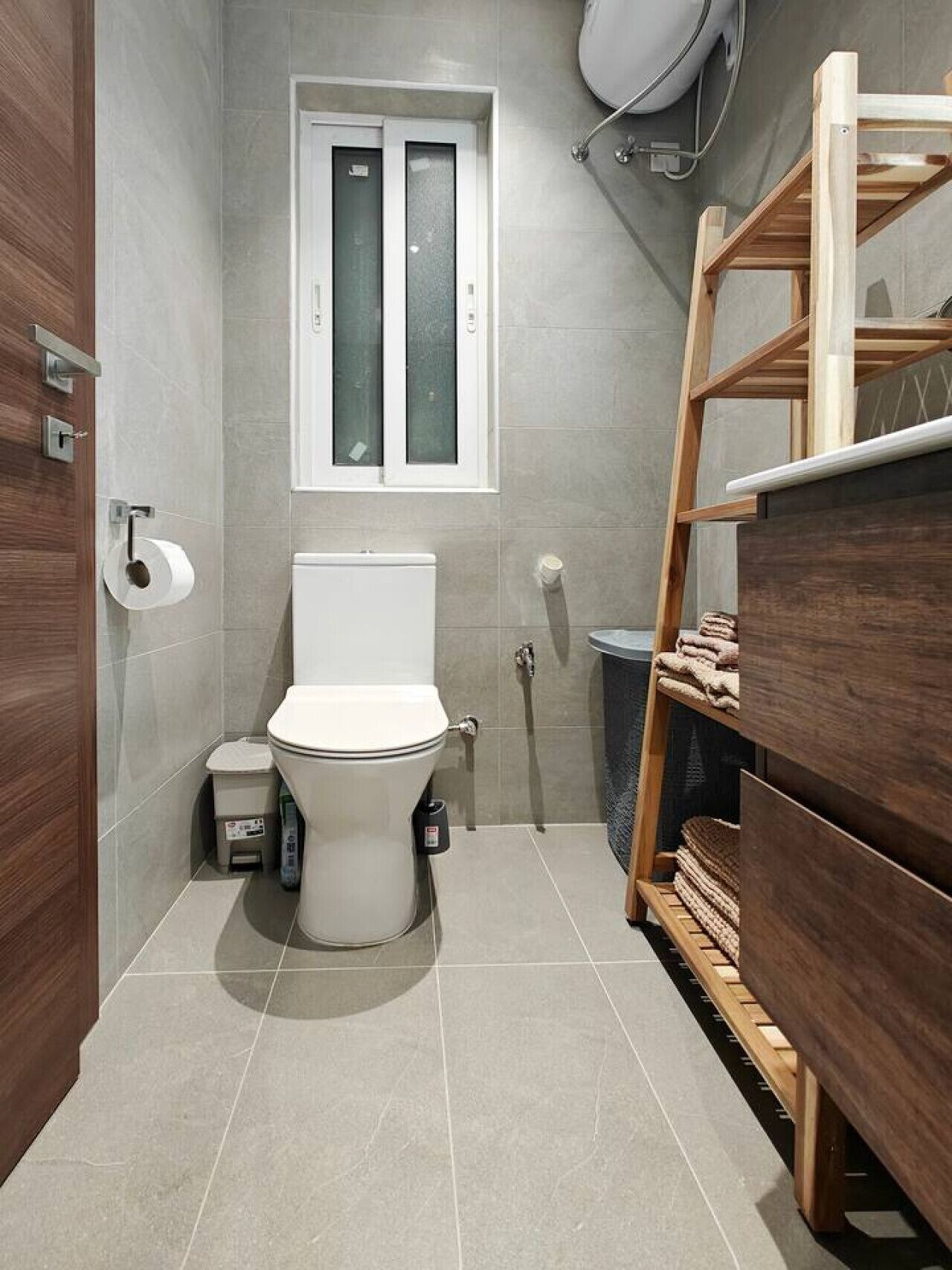 Ein kleines Badezimmer mit Toilette, einem Fenster und einer Holzauslage mit Handtüchern.