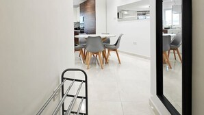 A modern kitchen with a central island, a dining area with a round table and chairs, and a large mirror on the wall. - Valley view 1  2 bedroom aparment (Luqa)