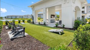 A modern building with a covered outdoor area, a lawn, and a water feature in the background. - Landing | Amazing 2BD, Pool, Clubhouse (Vero Beach)