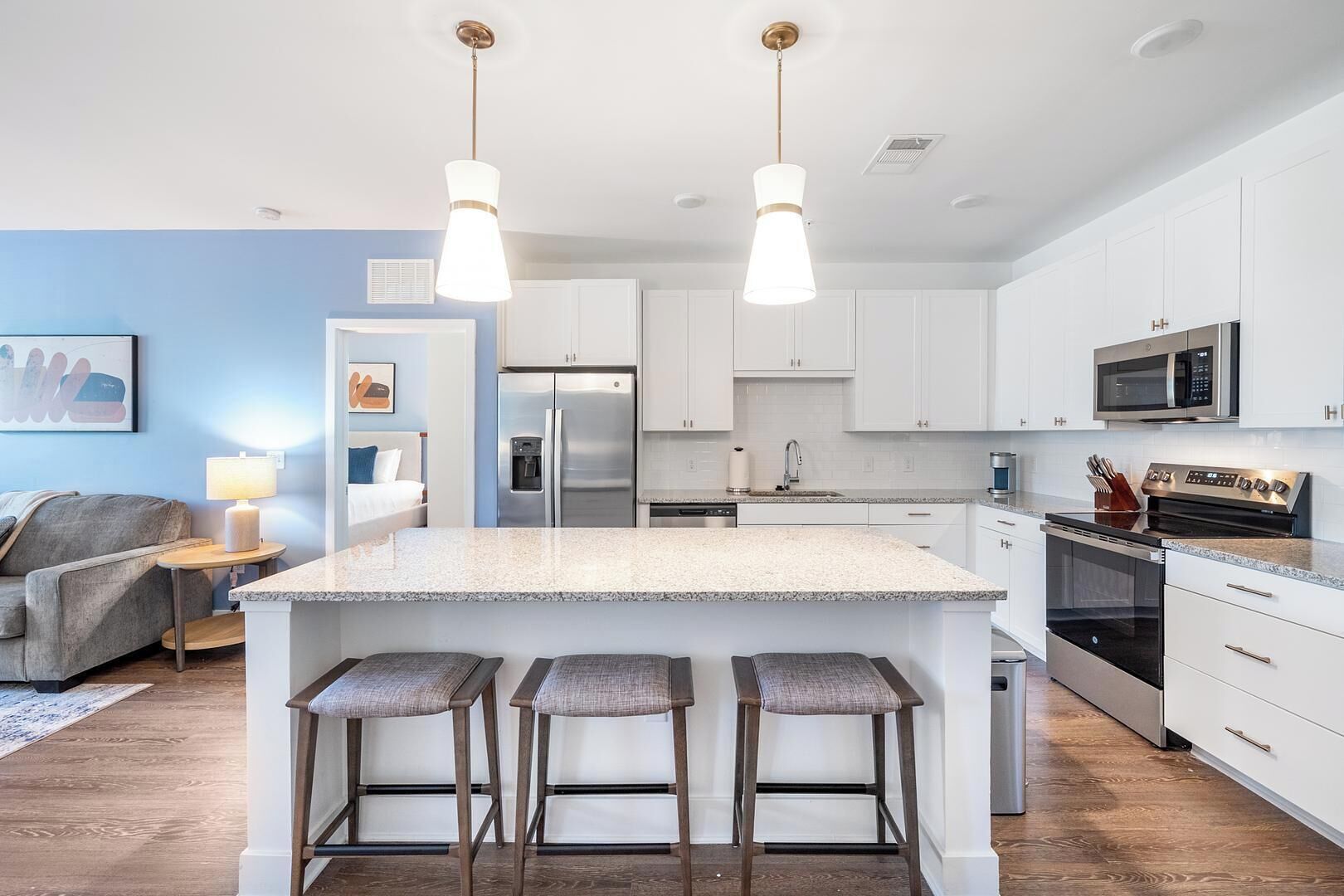 A modern kitchen with white cabinetry, a central island with bar stools, stainless steel appliances, and pendant lighting.