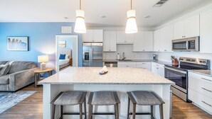 Une cuisine moderne dotée d’un îlot central, d’appareils électroménagers en acier inoxydable et de luminaires suspendus.