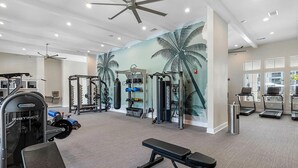 Une salle de sport équipée d’appareils de musculation Nautilus et Instinct, ornée d’une grande fresque murale représentant des palmiers et dotée d’un ventilateur de plafond.
