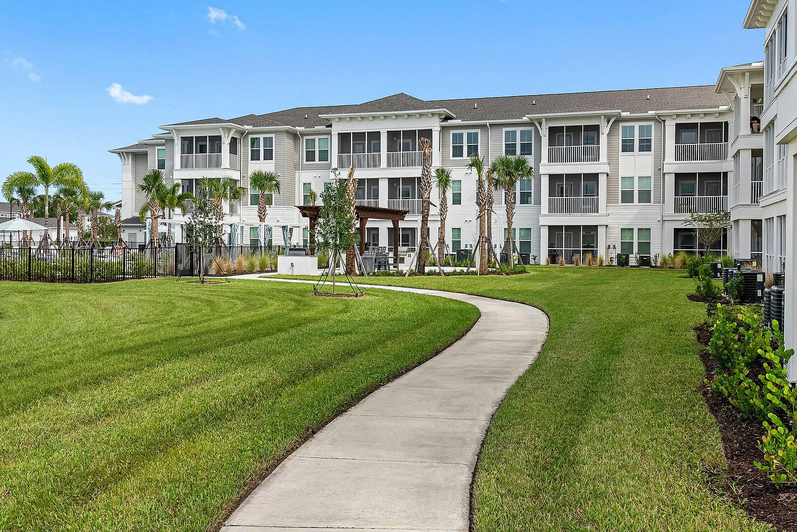 A modern multi-story residential building with a central courtyard, a curved pathway, and surrounding greenery.