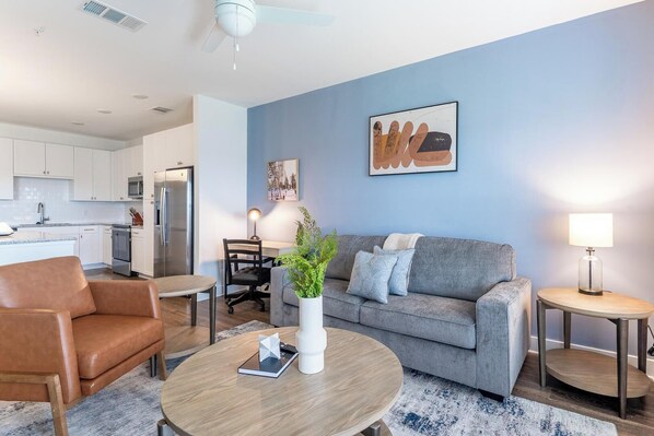 A modern living room with a grey sofa, a brown leather chair, a wooden coffee table, and a small side table with a lamp. - Landing | Incredible 2BD, Clubhouse, Gym (Vero Beach)