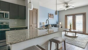 A modern kitchen with granite countertops, stainless steel appliances, and a central island with bar stools. - Landing | Incredible 1BD, Pool, Clubhouse (Houston)