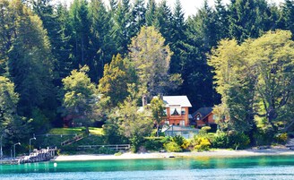 Una casa con muelle y playa, rodeada de un bosque frondoso.