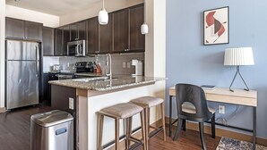 A modern kitchen with dark wooden cabinets, stainless steel appliances, a granite countertop, and a small bar area with stools. - Landing | Amazing 1BD, Pool, Gym (Houston)