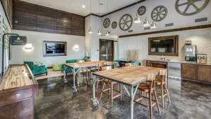 Um quarto espaçoso com mesa de bilhar, assentos estofados verdes, uma mesa de jantar de madeira e uma área de cozinha com uma grande janela e uma cafeteira.