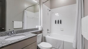 Et moderne badeværelse med bordplade i granit, et hvidt toilet, et badekar og en bruseniche.