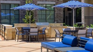 Een terras buiten met een barbecue, stoelen en parasols.
