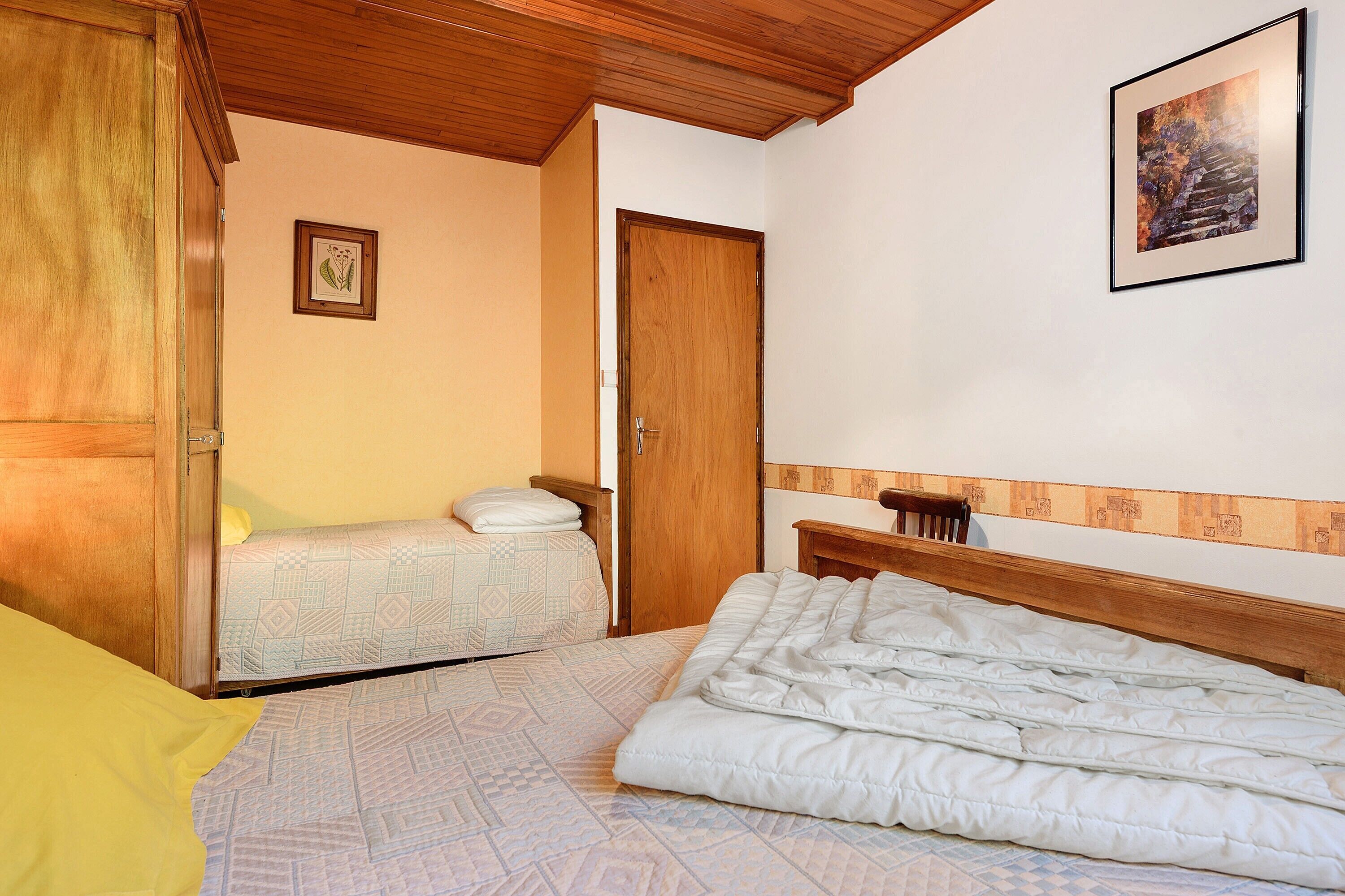 Quarto com cama, mesa de cabeceira, guarda-roupa de madeira, porta e um quadro na parede.