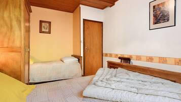Quarto com cama, mesa de cabeceira, guarda-roupa de madeira, porta e um quadro na parede.