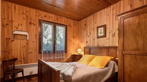 Een slaapkamer met houten lambrisering, een bed, een stoel, een nachtkastje en een garderobe.
