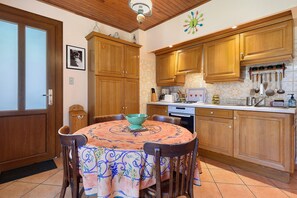 Une cuisine avec des meubles de rangement en bois, une table à manger avec des chaises et une machine à café.