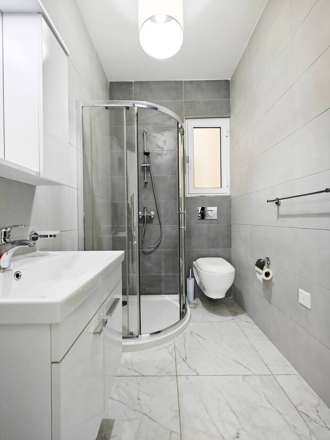 Ein modernes Badezimmer mit einer Duschkabine, einem weißen Waschbecken und einer Toilette.