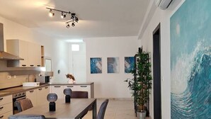 Une cuisine moderne avec des meubles blancs, un coin repas doté d’un sol en marbre et un grand tableau abstrait accroché au mur.