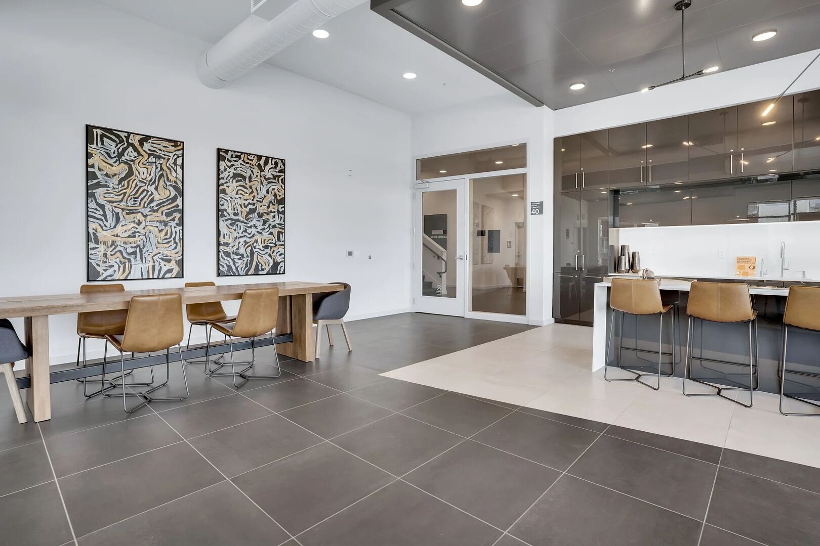 A modern dining area with a long wooden table, several chairs, and two abstract paintings on the wall.