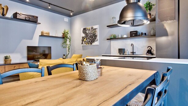 Una cocina moderna con estufa integrada, un lavamanos y una zona de comedor con mesa de madera y sillas azules.