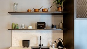 Una cocina con encimera de mármol, un lavamanos negro, una tetera y ollas de cobre en un estante.