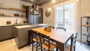 Una cocina moderna con una isla central, iluminación colgante y un comedor con una mesa y sillas de madera.