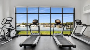 Une salle de sport équipée de deux tapis de course et d’un appareil elliptique, avec de grandes fenêtres donnant sur un lac.