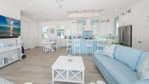 Een moderne keuken met witte kasten, een centraal eiland en een eetgedeelte met witte stoelen.