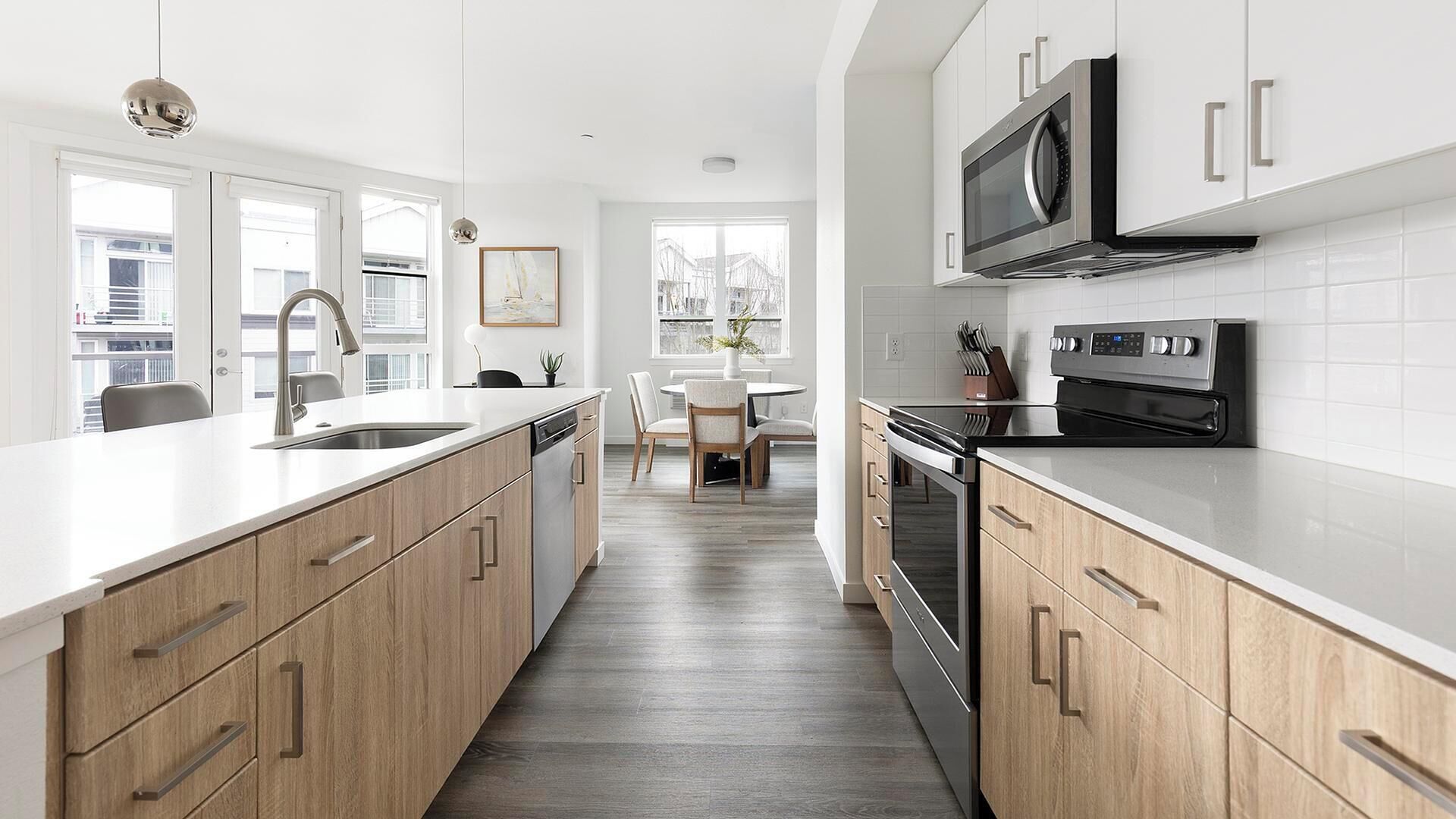 A modern kitchen with white cabinets, stainless steel appliances, and a wooden floor.
