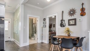 Ein Essbereich mit Holztisch, schwarzen Stühlen, einer Gitarre und einer Wanduhr im Sonnenstrahlendesign.