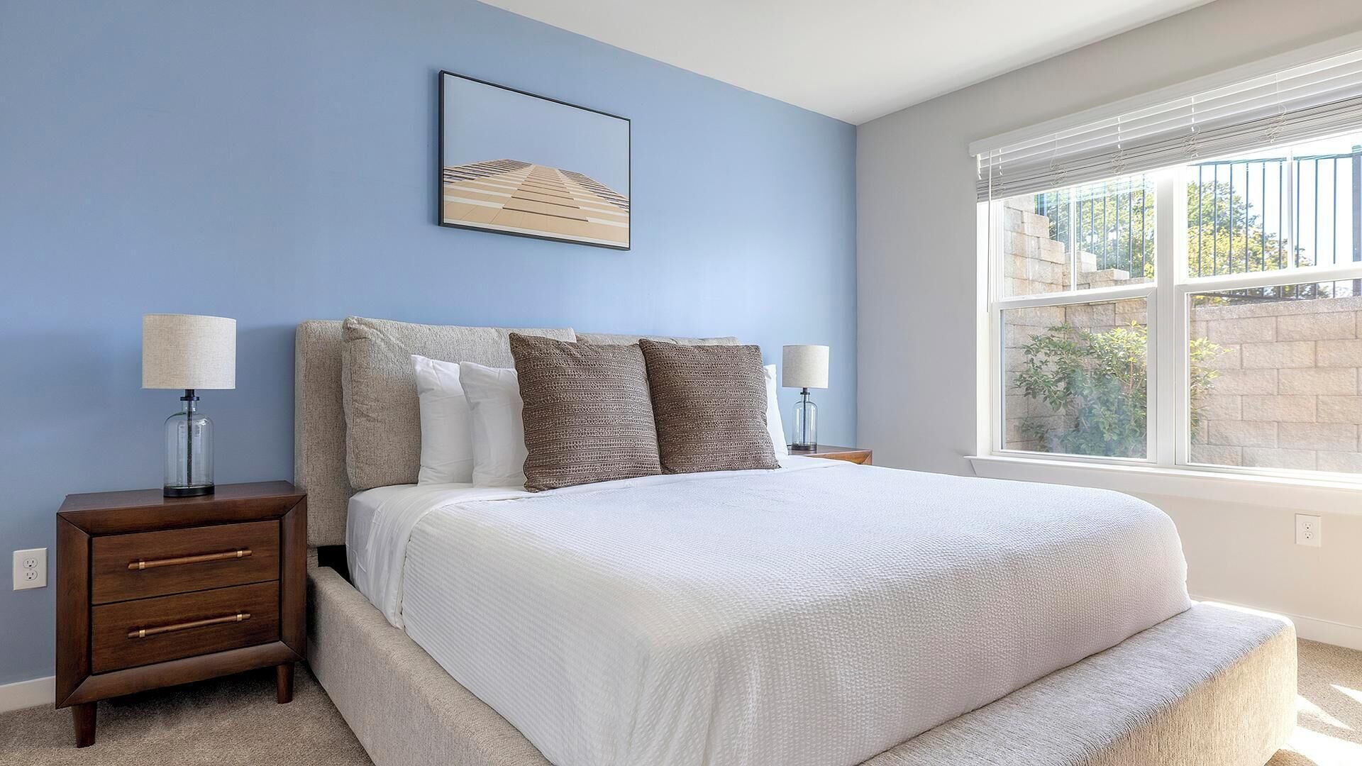 A bedroom with a bed, two nightstands, a window, and a wall-mounted picture.