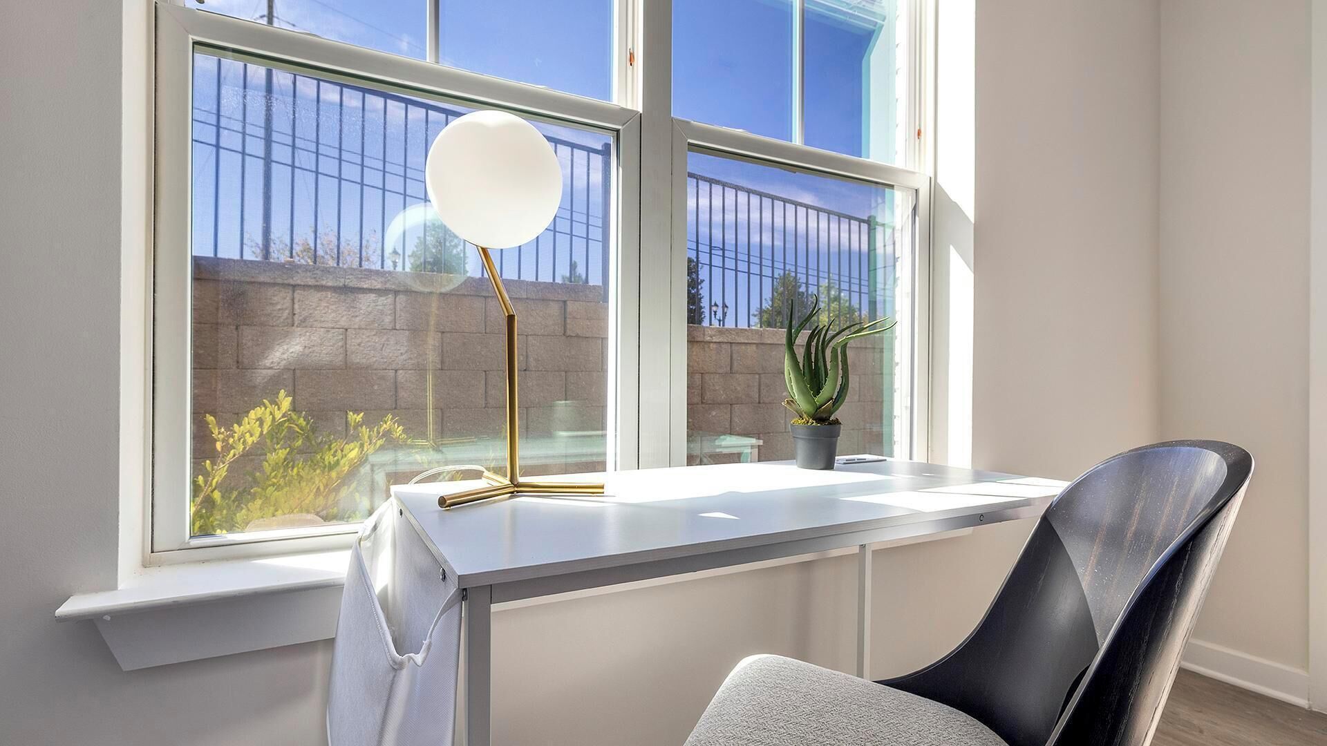 A modern room with a desk, a chair, a window with a view of a building and a plant.