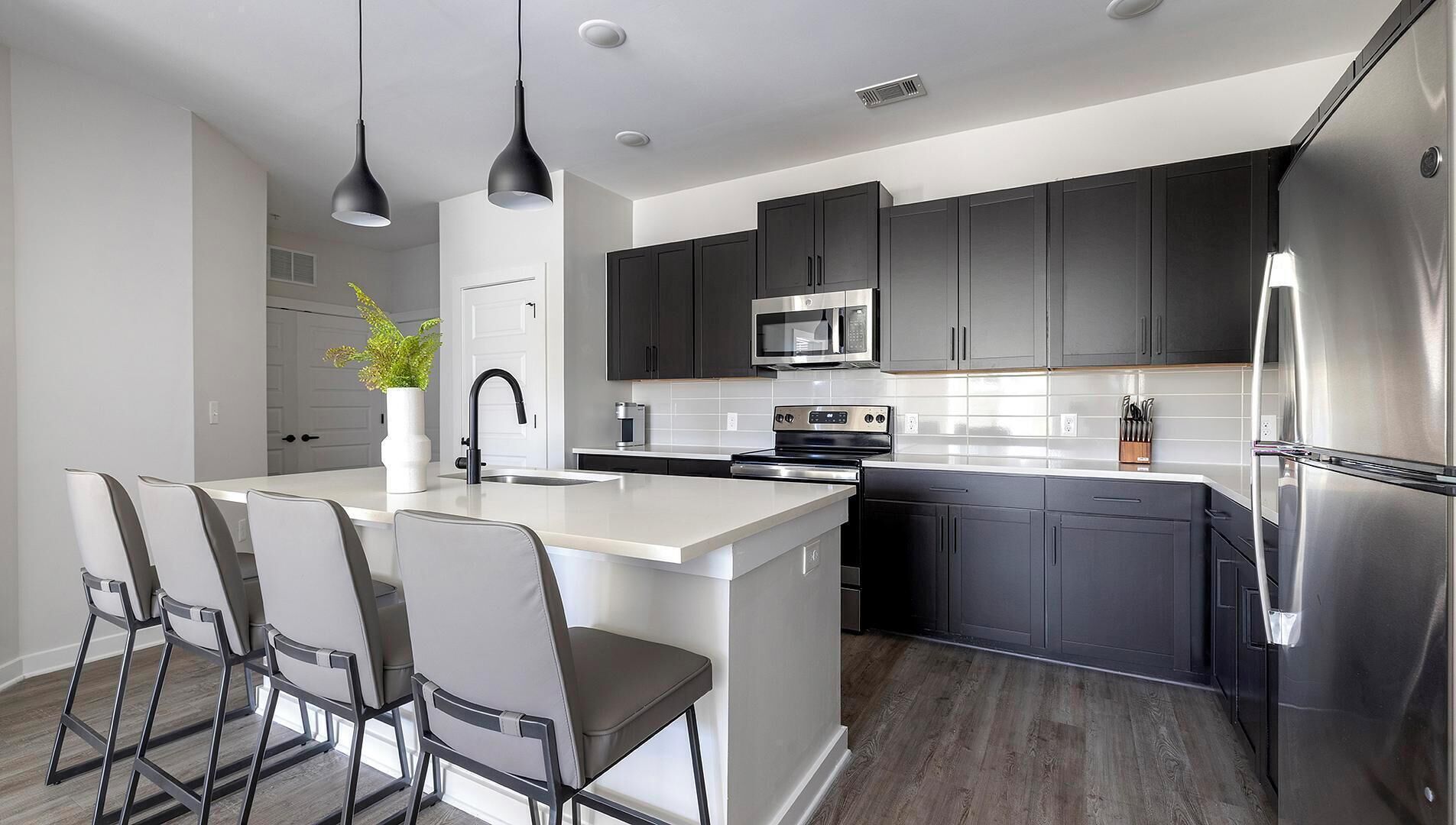 A modern kitchen with dark cabinets, stainless steel appliances, and a central island with bar stools.