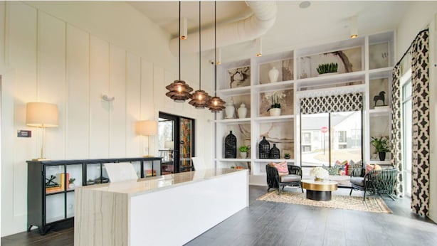 Een moderne keuken met een centraal eiland, hangende verlichting en een uitzicht op buiten door grote ramen.