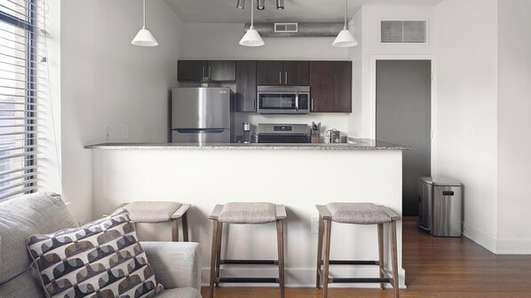 A modern kitchen with stainless steel appliances, a bar area with stools, and a window with blinds. - Landing | Chic 1BD, Clubhouse, Gym (Richmond)