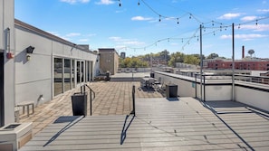 A rooftop terrace with outdoor seating, a trash bin, and string lights. - Landing | Chic 1BD, Clubhouse, Gym (Richmond)