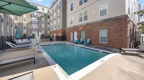 A swimming pool with lounge chairs and umbrellas, surrounded by multi-story buildings with brick and siding exteriors. - Landing | Chic 1BD, Clubhouse, Gym (Richmond)