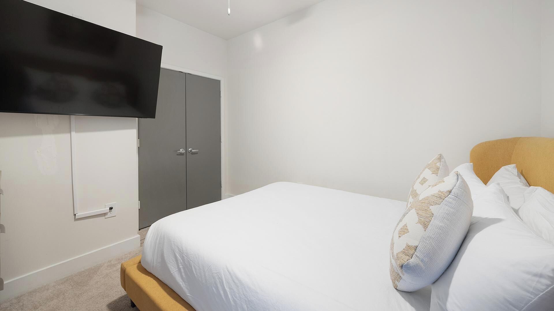 A bedroom with a bed, a wardrobe, and a flat-screen TV mounted on the wall.