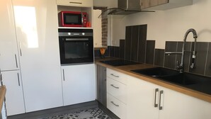 Et køkken med hvide skabe, en sort bordplade, en rød mikrobølgeovn og en sort ovn.