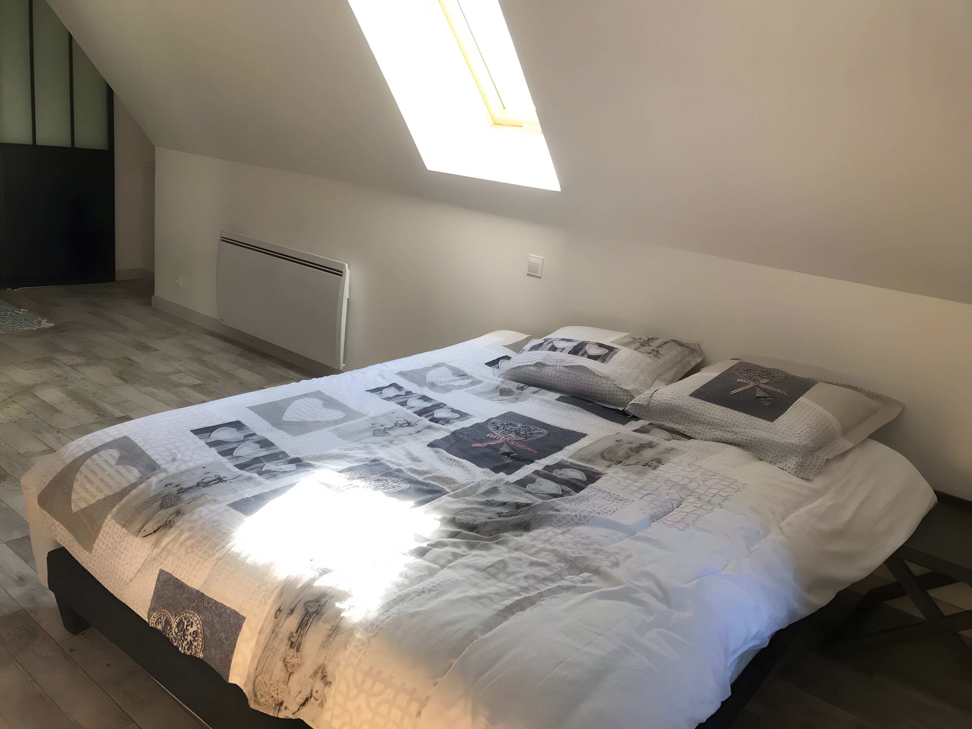 Une chambre à coucher avec un lit, une lucarne, un radiateur et un plancher en bois.