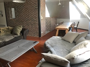 Un espace de vie avec un mur en briques, une table à manger en bois et un canapé agrémenté de coussins.