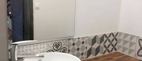 Une salle de bain avec un lavabo blanc, un plan de toilette en bois et des carreaux décorés.