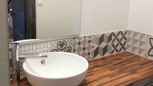 Une salle de bain avec un lavabo blanc, un plan de toilette en bois et un mur recouvert de carreaux décoratifs.
