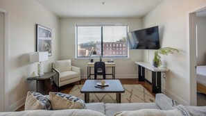 A compact living space with a sofa, a small table, a chair, a desk, and a TV mounted on the wall. - Landing | Incredible 2BD, Courtyard (Richmond)