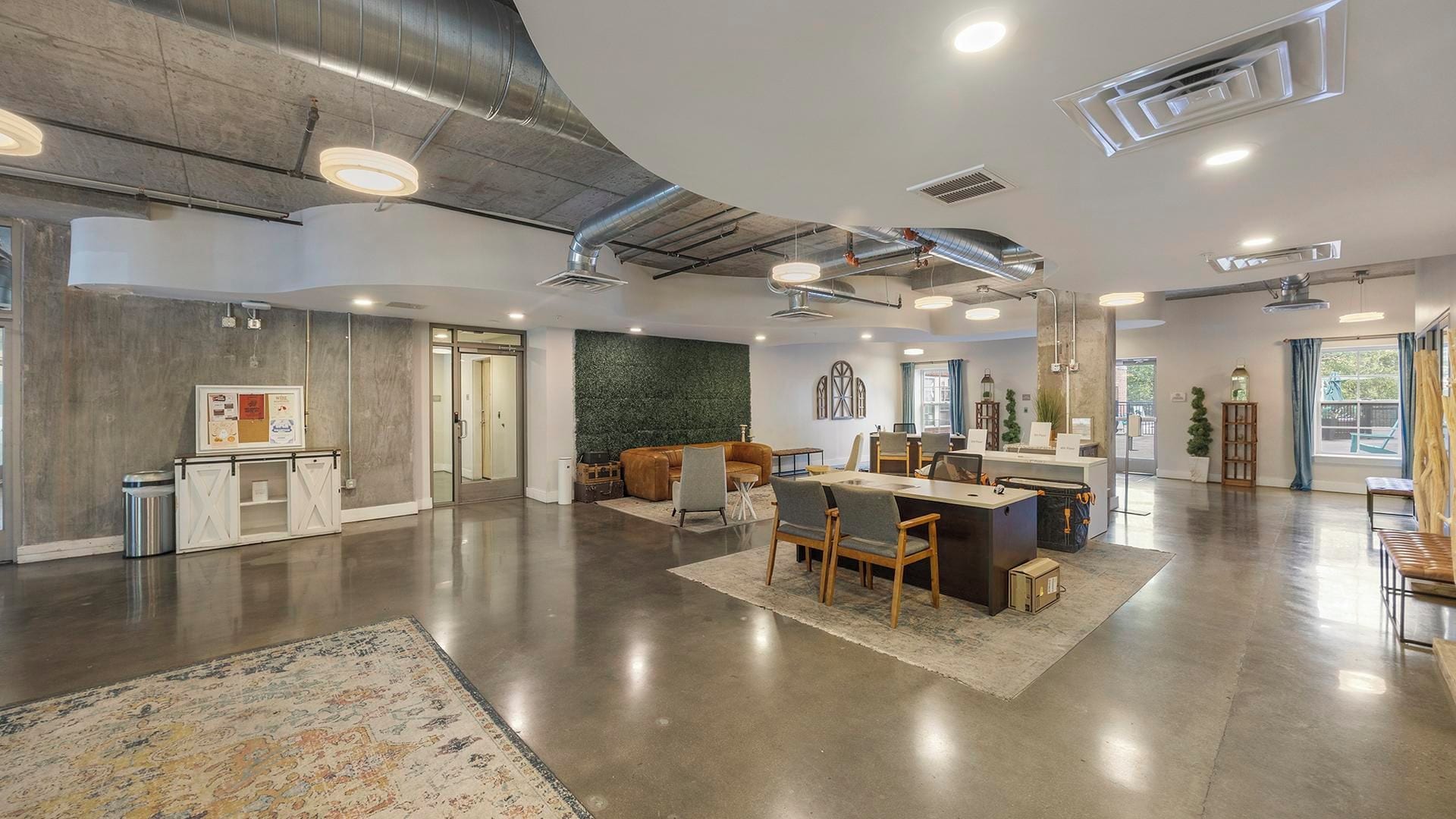 A spacious, modern interior with a central dining area, a reception desk, and a green accent wall.