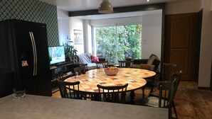 Eine moderne Küche mit einem runden Esstisch, Stühlen, einem Kühlschrank und einem großen Fenster mit Blick auf Grünflächen.