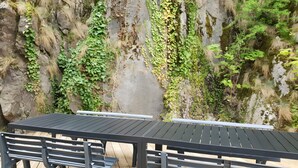 Eine Holzdar Terrasse mit einem Metalltisch und Bänken, umgeben von einer Steinsichtmauer mit Grünpflanzen.